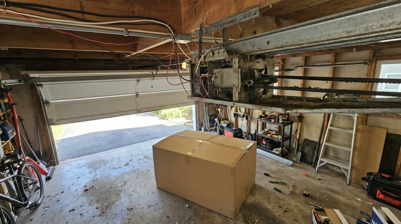 Old garage door opener with a new unit boxed on the floor below